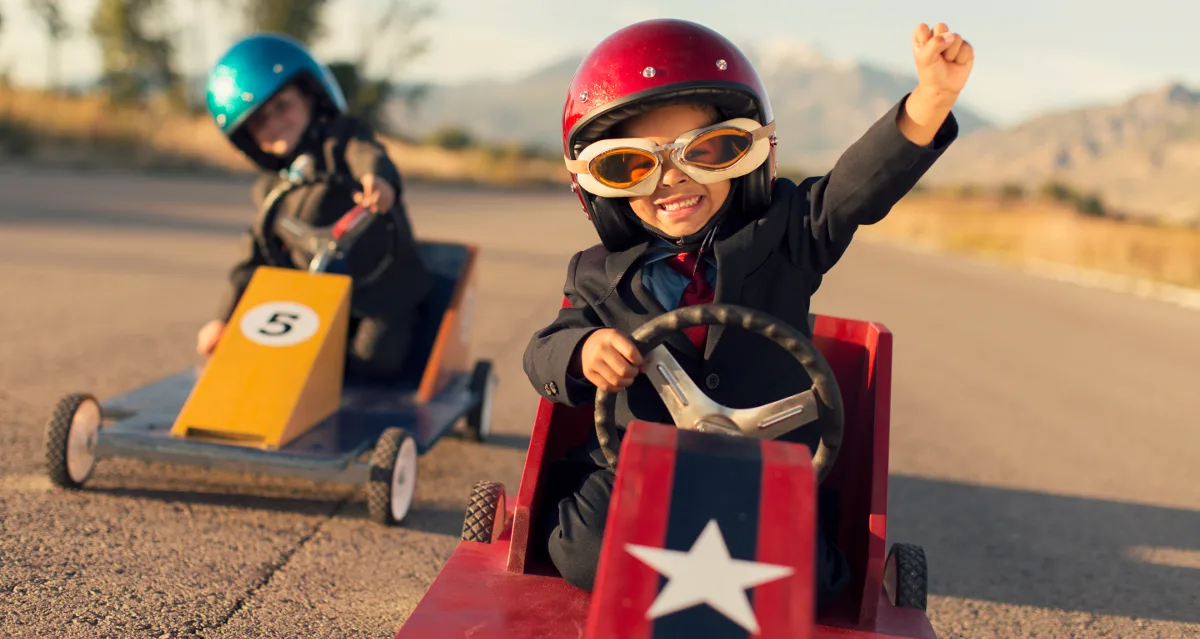 Zwei Kinder mit Helmen in Seifenkisten beim Rennen